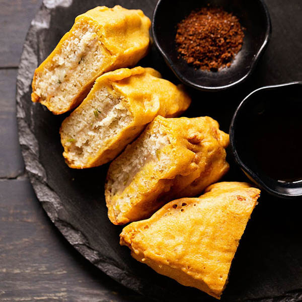 bread pakora triangles on a black round stone platter.