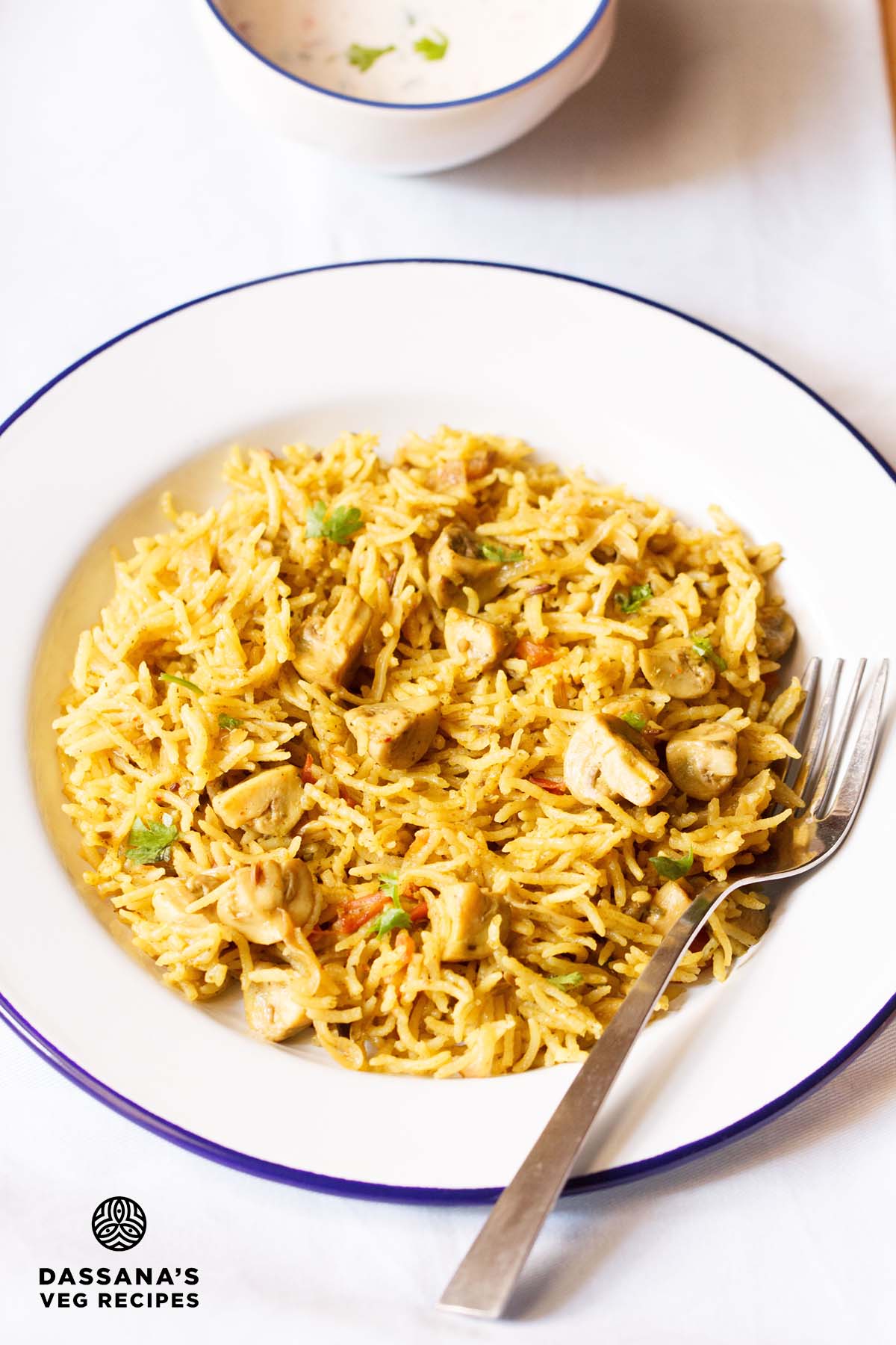 chettinad biryani on a blue rimmed white plate with a fork.