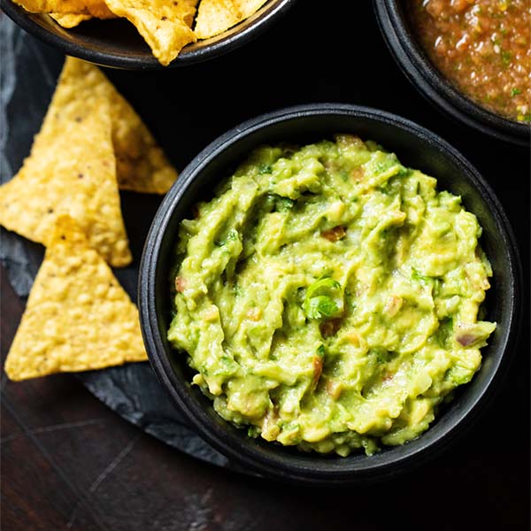 guacamole in a black bowl with nacho chips by side.