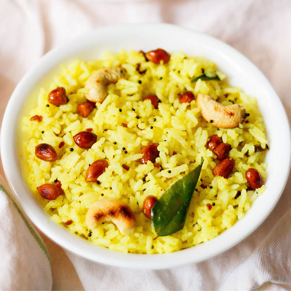 yellow colored lemon rice served in a white bowl on a white cotton cloth
