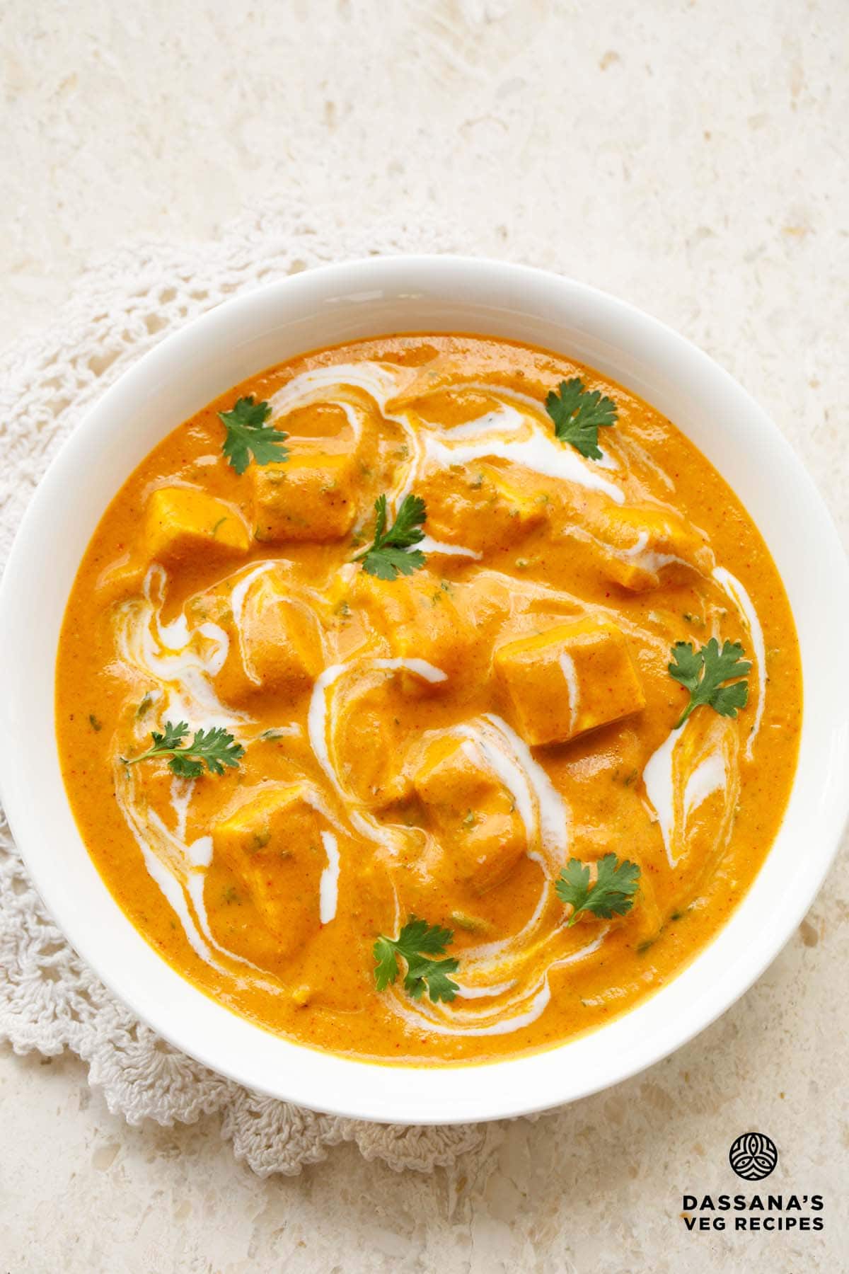 paneer angara in a white bowl garnished with coriander leaves and swirls of cream placed on an off-white doily.